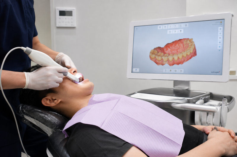 치과 진료 의자에 누운 환자의 구강을 구강 스캐너로 스캔하는 모습과 모니터에 나타난 3D 구강 모델