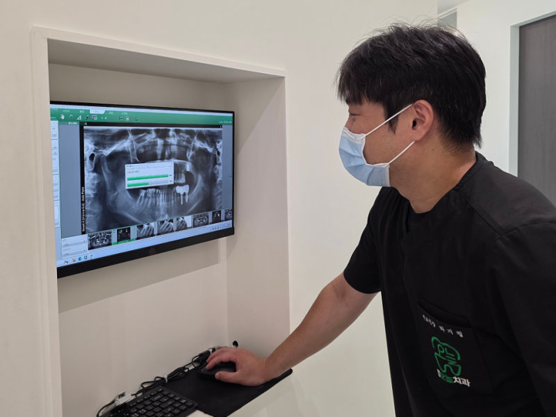 임플란트 뼈이식, 꼭 필요한가요? 뼈가 없으면 임플란트 못하나요? 6 마스크 쓴 의사가 모니터로 치아 엑스레이를 보고 있다.